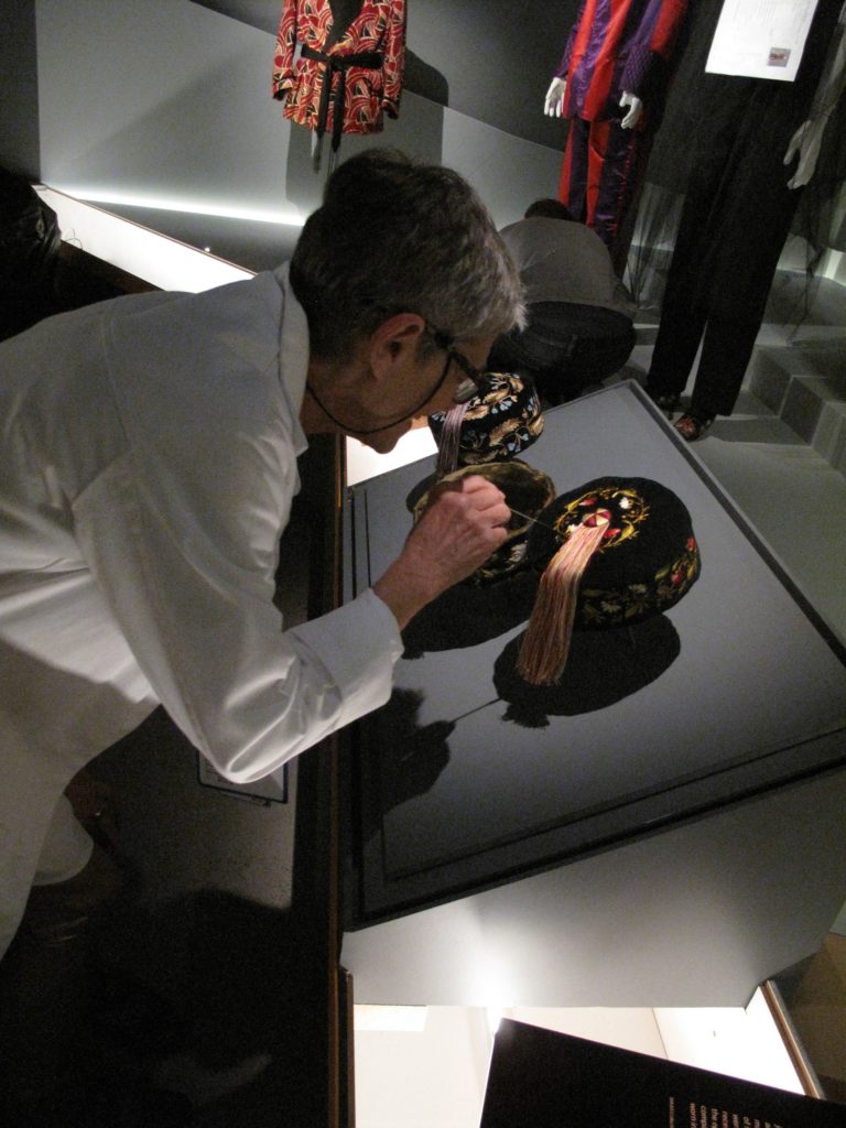 Kaye Spilker, Curator, straightening the silk tassels of the Smoking caps